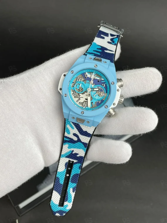 Hublot Big Bang Blue Camo, açık mavi kasalı, transparan kadranlı, kamuflaj desenli kayışlı, quartz mekanizmalı spor tarz replika saat modeli