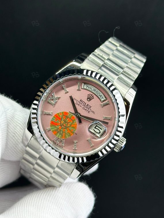 Rolex Day-Date paslanmaz çelik kasa, pembe kadran, President bilezik, yivli bezel ve gün/tarih göstergeli yakın çekim görseli - Erişilebilir klasik lüks saat