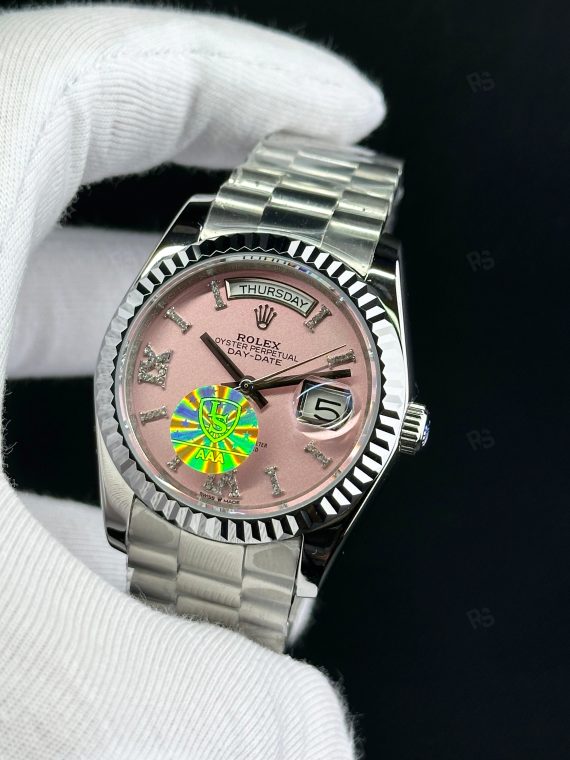 Rolex Day-Date paslanmaz çelik kasa, pembe kadran, President bilezik, yivli bezel ve gün/tarih göstergeli yakın çekim görseli - Erişilebilir klasik lüks saat