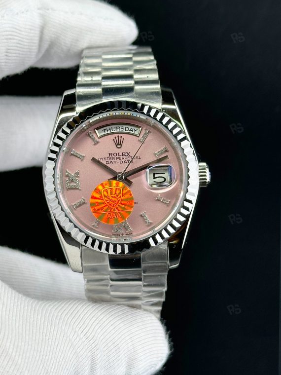 Rolex Day-Date paslanmaz çelik kasa, pembe kadran, President bilezik, yivli bezel ve gün/tarih göstergeli yakın çekim görseli - Erişilebilir klasik lüks saat
