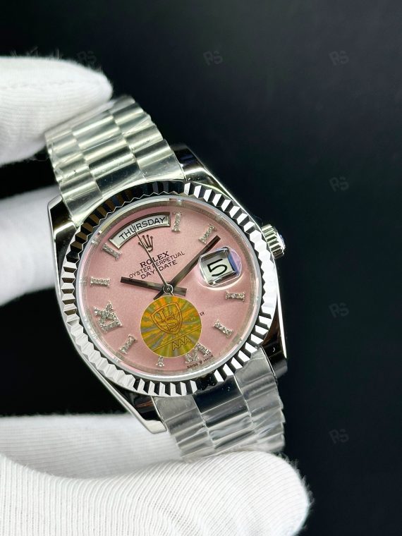 Rolex Day-Date paslanmaz çelik kasa, pembe kadran, President bilezik, yivli bezel ve gün/tarih göstergeli yakın çekim görseli - Erişilebilir klasik lüks saat
